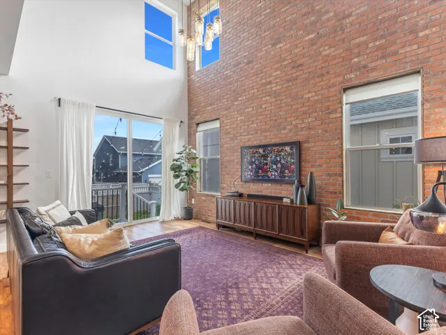 Double-height living area featuring an exposed brick accent wall, floor-to-ceiling windows, and a multi-light pendant fixture