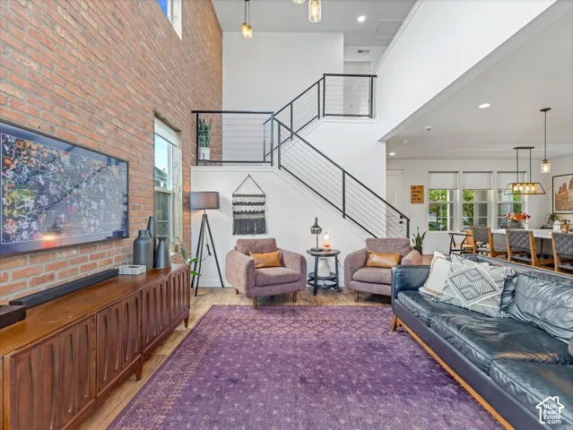 Double-height living area featuring an exposed brick feature wall, hardwood flooring, and a metal staircase with horizontal cable railings