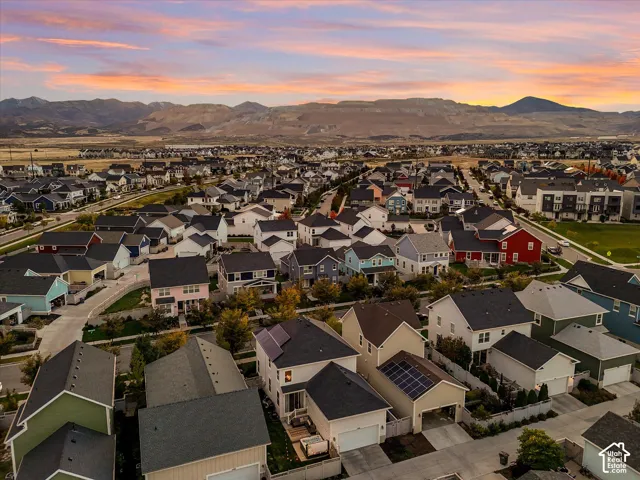 Aerial perspective of a multi-level residence featuring integrated rooftop solar panels, a two-car garage, a fenced rear yard, and mountain backdrops