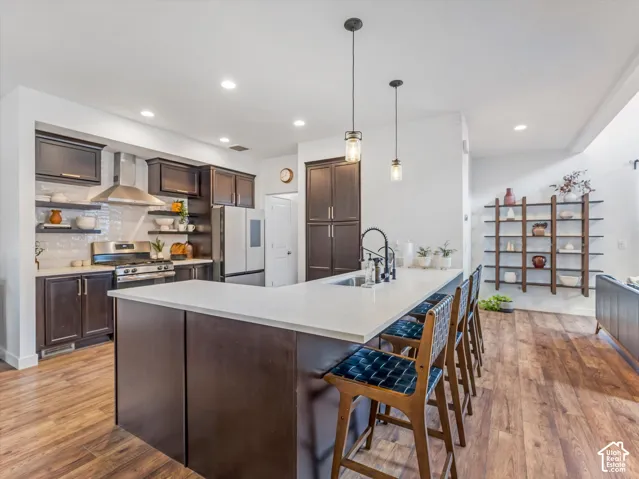 Kitchen featuring a central island with a solid surface countertop, dark-toned cabinetry, stainless steel appliances, wood-finish flooring, and open shelving