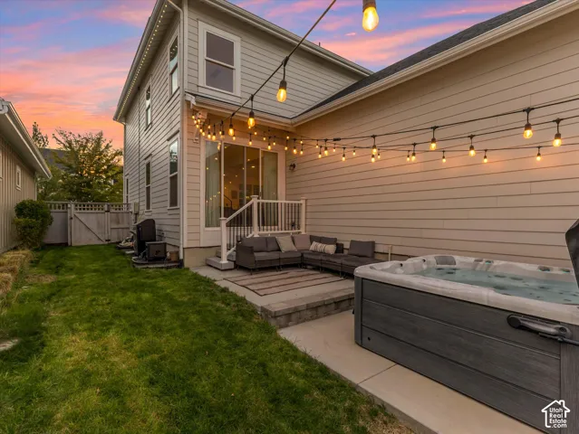 Rear exterior featuring horizontal lap siding, a concrete patio, an integrated hot tub, and overhead string lighting