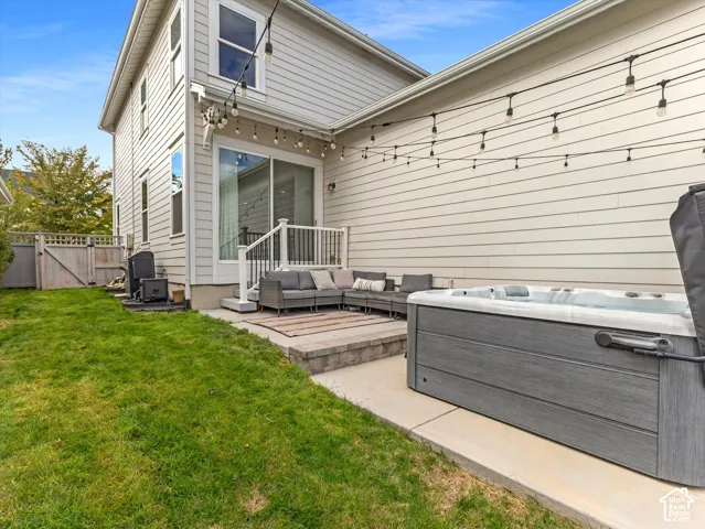 Rear exterior featuring light-toned horizontal siding, a concrete patio, built-in hot tub, and wood-style fencing