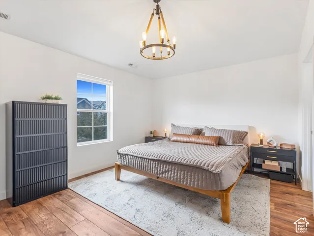 Primary bedroom featuring wood-finish flooring, a multi-light metal chandelier, and a large single-hung window with a grid pattern
