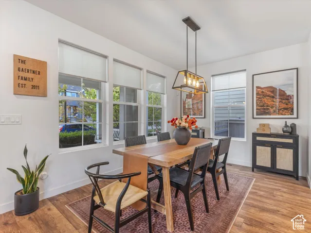 Dining area featuring wood-finish flooring, large windows with roller shades, and a linear four-light metal pendant fixture
