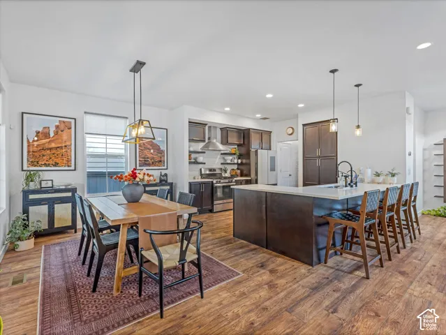 Open-concept kitchen and dining area featuring wood-finish flooring, dark-toned cabinetry, a spacious kitchen island with stone-surface countertop, and stainless steel appliances