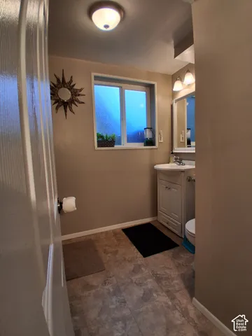 Bathroom featuring a vanity cabinet with a basin sink, wall-mounted mirror, sliding window, and neutral-toned floor tile
