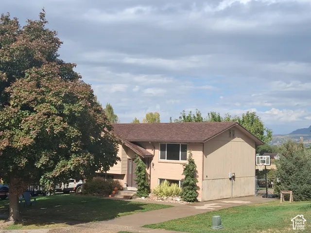 Split-level exterior featuring tan brick and neutral siding, asphalt shingle roofing, paved driveway, and mature landscaping