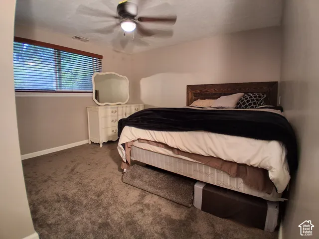 Neutral wall tones, wall-to-wall carpeting, window with wood-finish blinds, and a ceiling-mounted light fixture with a fan
