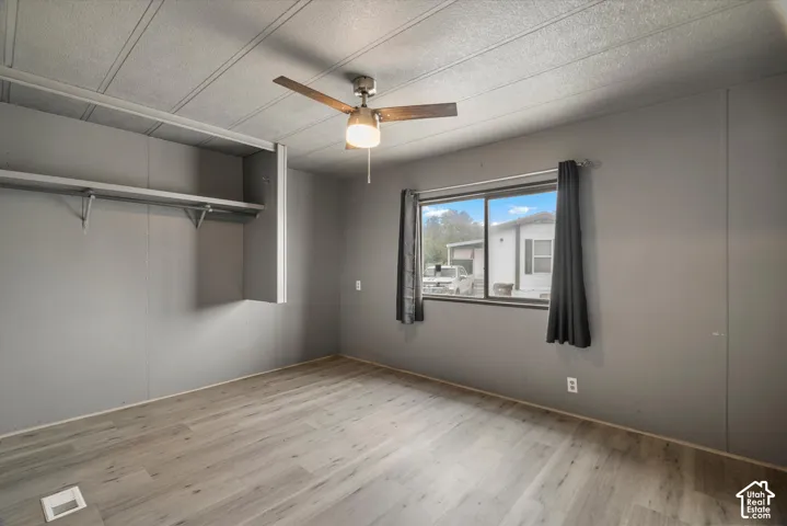 Neutral-toned interior room featuring wood-finish flooring, a ceiling fan with integrated lighting, and built-in wall shelving