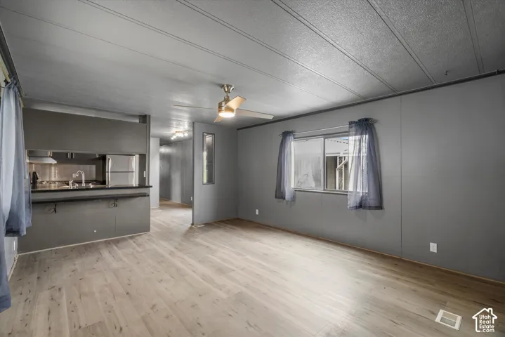 Open-concept interior featuring wood-finish flooring, a kitchen pass-through, neutral wall tones, and a ceiling fan with integrated lighting