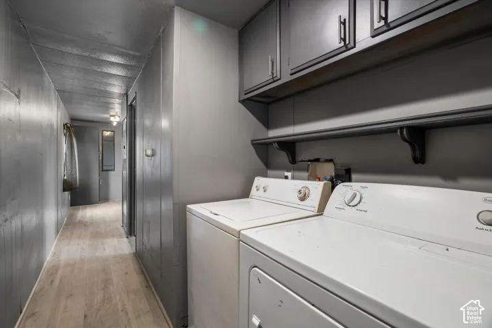 Laundry area featuring light-toned wood-finish flooring, charcoal-toned wall-mounted cabinetry, and an open display shelf