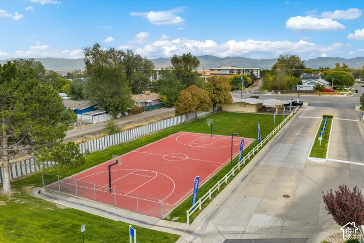 Paved basketball court with permanent hoops, chain-link fencing, expansive manicured lawn, and mountain backdrop