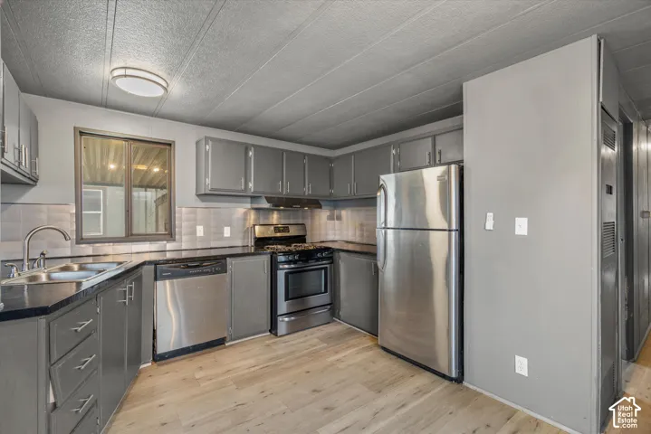 Kitchen featuring grey cabinetry, dark countertops, wood-finish flooring, and stainless steel appliances including a range, dishwasher, and refrigerator