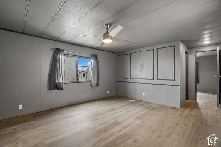 Interior space featuring wood-finish flooring, paneled wall detailing, and a ceiling-mounted light fixture with integrated fan