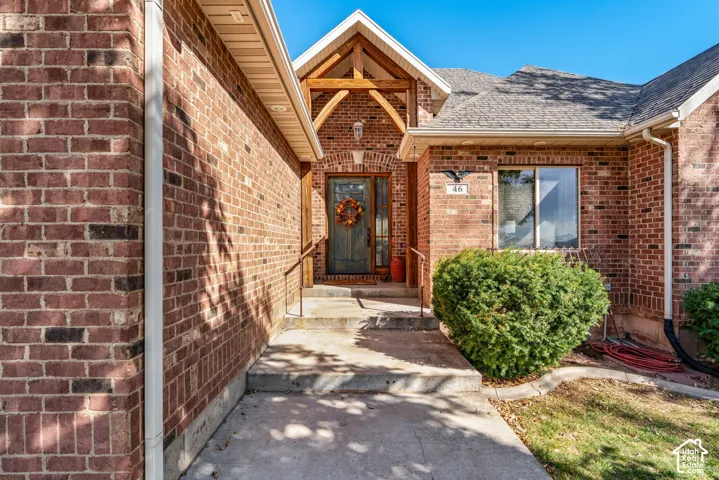 Red brick exterior featuring a covered entryway with timber-framed gables, concrete steps, and a glass-paneled front door