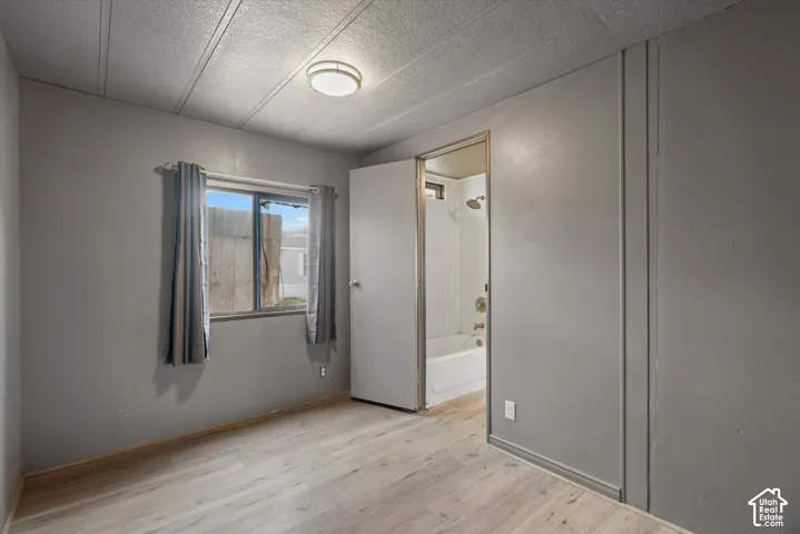 Room featuring light wood-finish flooring, a neutral grey color palette, flush-mount ceiling lighting, and a single sliding window