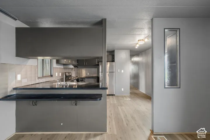 Kitchen featuring a breakfast bar with a solid surface countertop, wood-finish flooring, stainless steel appliances, and integrated ceiling track lighting