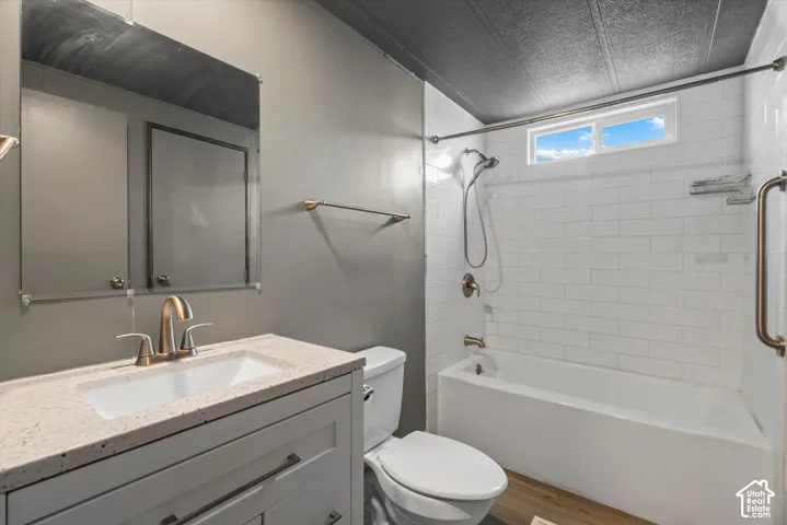 Bathroom featuring a vanity with a light-toned speckled countertop, an undermount sink, a tub-shower combination with white subway tile surround, a handheld shower fixture, and a transom window