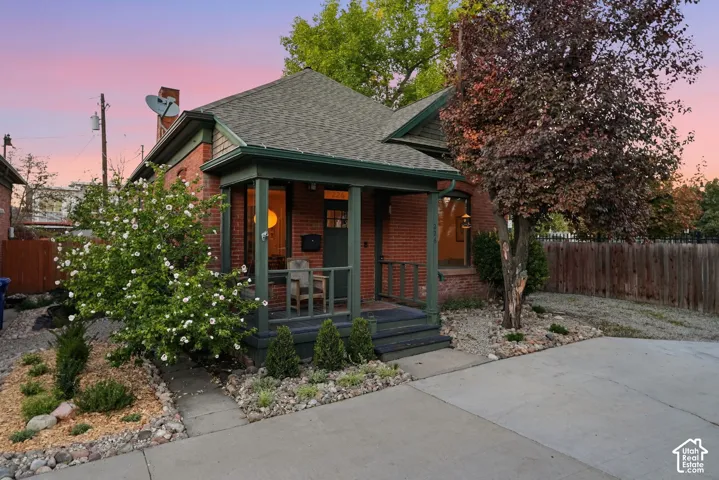 Brick exterior featuring a covered front porch, asphalt shingle roofing, and landscaped rock gardens