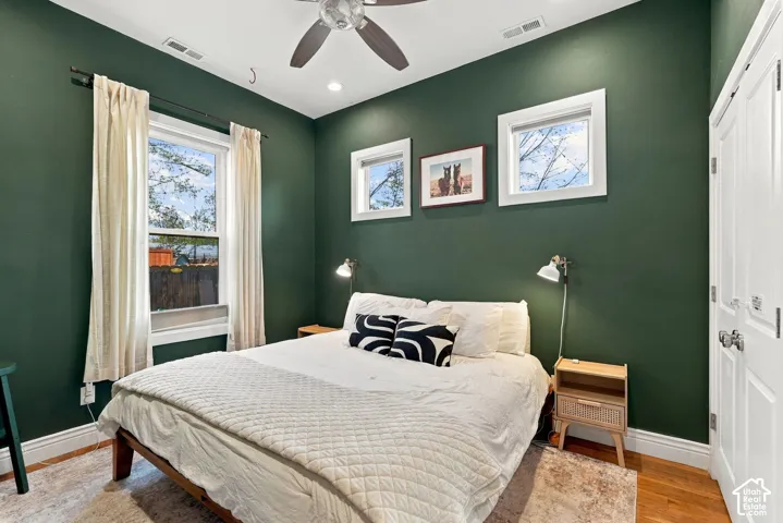 Room with wood-finish flooring, dual wall-mounted light fixtures, multi-pane windows, and a ceiling fan