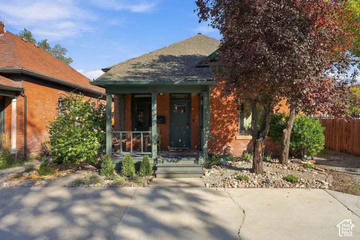 Brick exterior residence featuring a covered front porch, shingled gable roof, and rock-mulched landscaping