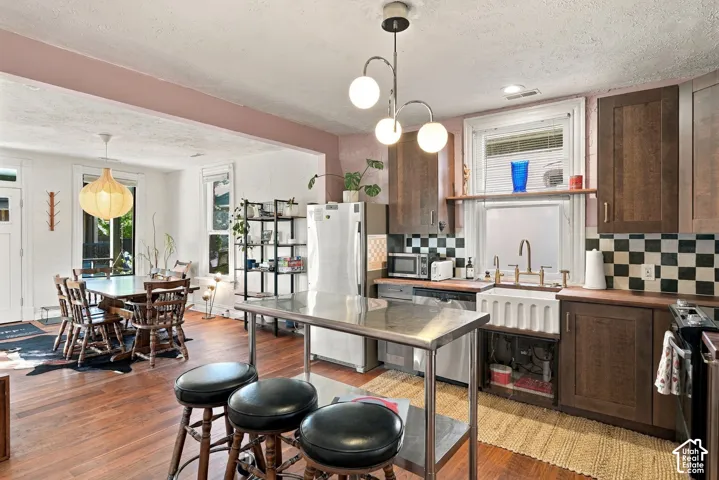 Kitchen featuring dark wood-finish cabinetry, a farmhouse-style apron sink with a brass-finish faucet, a checkerboard-patterned tile backsplash, and wood-finish flooring