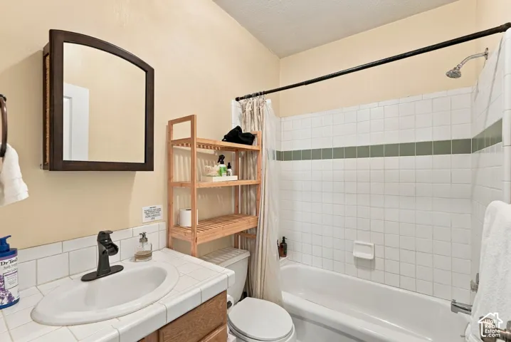 Bathroom featuring a tiled vanity countertop with a drop-in sink, a wall-mounted medicine cabinet with a wood frame, and a tub-shower combination with decorative tile inlay