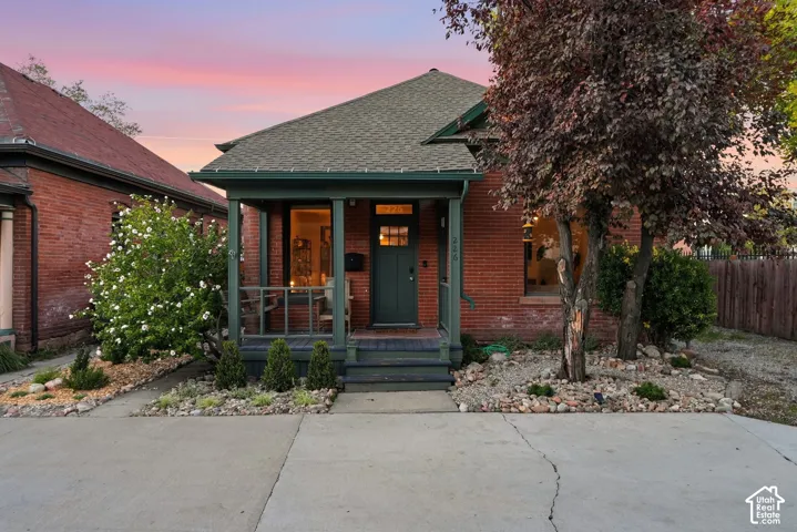 Classic brick exterior featuring a covered front porch, gabled roofline, and landscaped rock garden beds