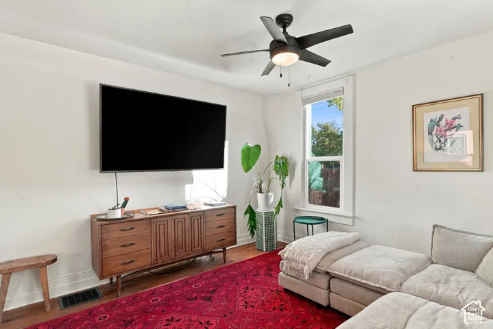 Living space featuring wood-finish flooring, a ceiling fan with integrated lighting, and a window with white trim