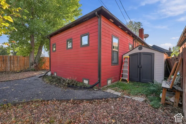 Horizontal wood-plank siding, metal rain gutters, and exterior-mounted storage unit situated on a gravel lot