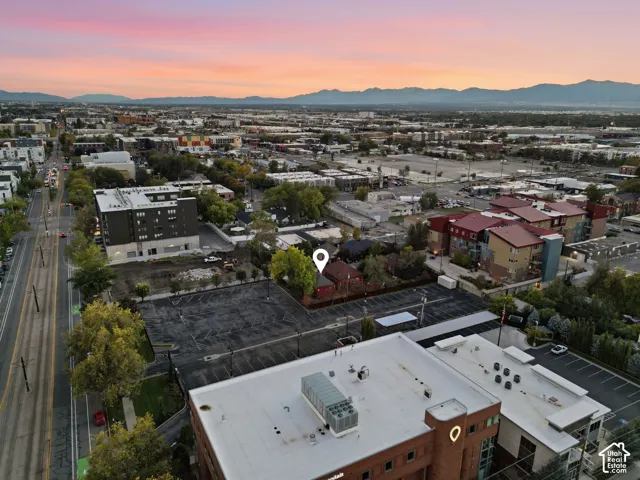 Aerial perspective of property featuring a detached structure with a pitched roof, mature trees, and paved surface parking