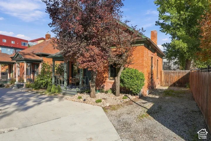 Red brick exterior featuring a covered front porch, gabled roofline, concrete driveway, and rock-based landscaping