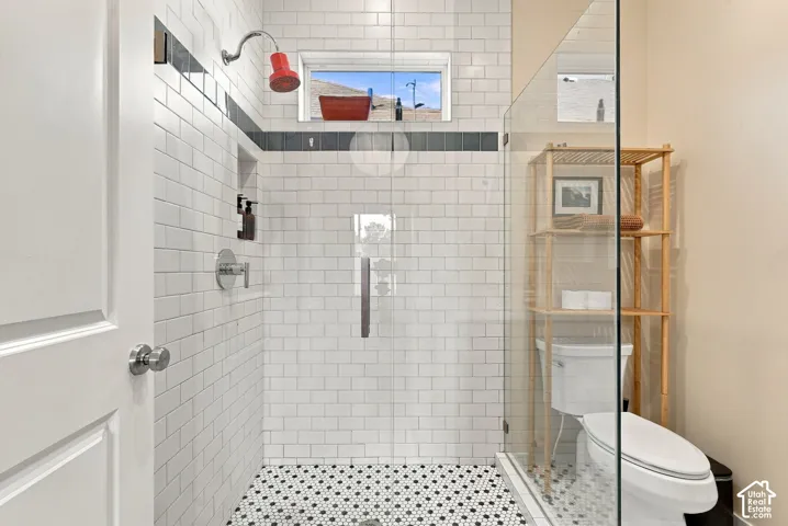 Walk-in shower featuring subway tile walls, a decorative dark tile accent border, glass partition, integrated wall niche, and hexagonal floor tile