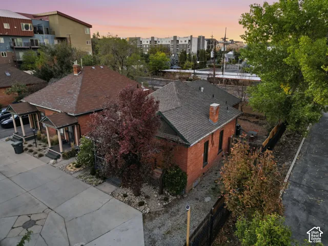 Brick exterior featuring a hip roof, covered porch, masonry chimneys, and mature landscaping