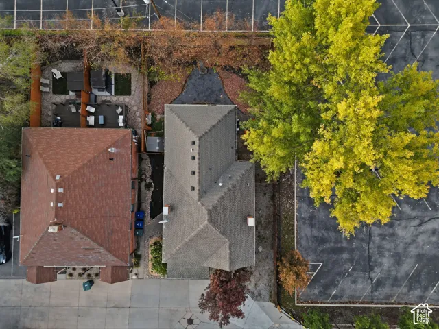 Aerial perspective of the property featuring a shingled roof, a paved patio area, wood fencing, and mature trees