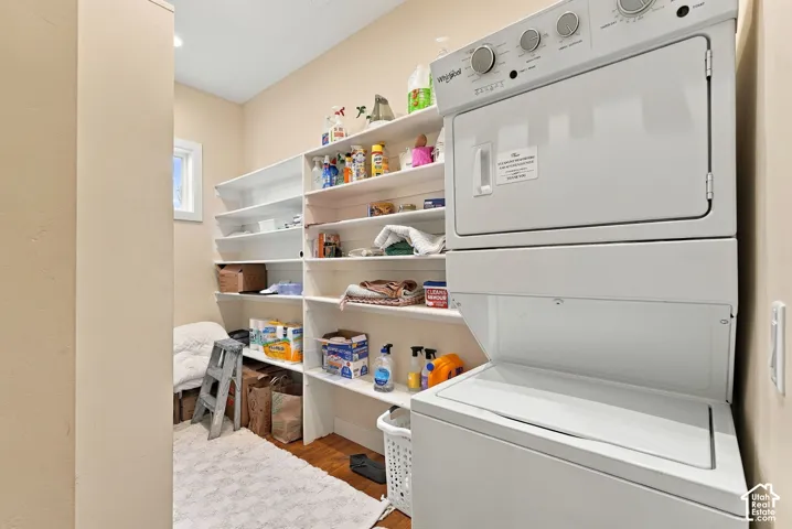Laundry area featuring a white stackable washer and dryer unit, multi-level wall-mounted shelving, and wood-finish flooring