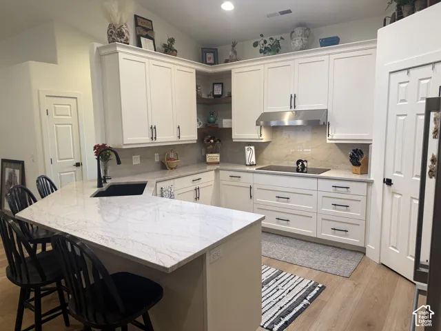 Kitchen featuring white cabinetry, stone-finish countertops, an undermount sink with a matte black faucet, a stainless steel range hood, and wood-finish flooring