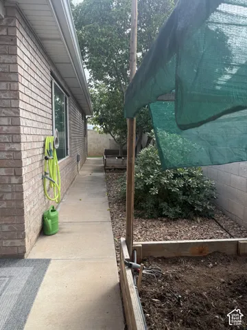Brick exterior side yard featuring a concrete walkway, elevated garden bed, stone ground cover, and block wall perimeter