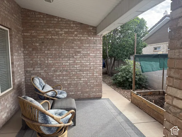 Covered patio with red brick masonry walls, concrete flooring, and an elevated wood garden planter