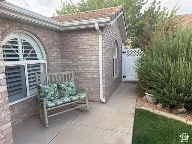Brick exterior featuring arched windows with white shutters, concrete patio, and a white privacy gate with lattice detailing