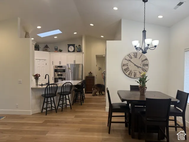 Vaulted ceilings with an integrated skylight, light-toned wood-finish flooring, built-in white cabinetry, recessed lighting, and a multi-arm chandelier