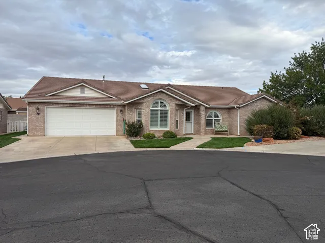 Single-level brick exterior featuring a tiled roof, multi-car garage, arched window accents, and a concrete driveway