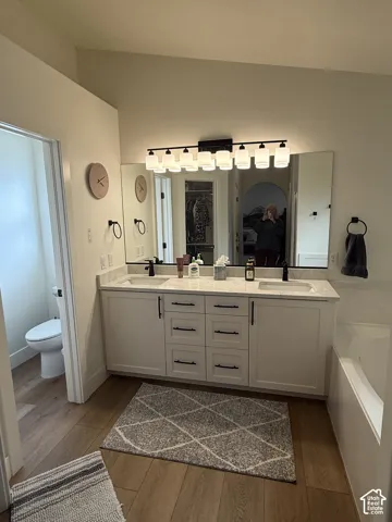 Dual-sink vanity with light-toned stone countertop, white shaker-style cabinetry, matte black hardware, and an expansive multi-light fixture
