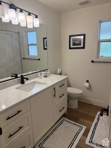 Bathroom featuring a white vanity with stone-style countertop, undermount sink, matte black hardware, large wall-mounted vanity mirror with multi-light fixture, and wood-finish flooring