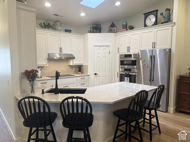 Kitchen featuring white shaker cabinetry, stone-finish countertops, stainless steel wall-mounted oven and microwave, recessed ceiling lighting, and a skylight