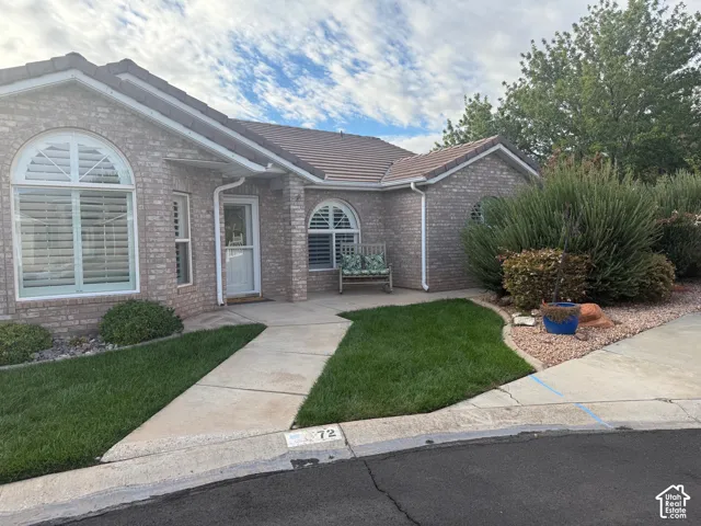 Brick exterior featuring a tile roof, arched windows, concrete walkway, and landscaped lawn