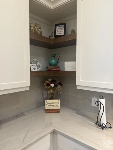 Corner shelving featuring dual wood-finish floating shelves, light-toned stone-surface countertops, full-height stone-surface backsplash, and white shaker-style cabinetry