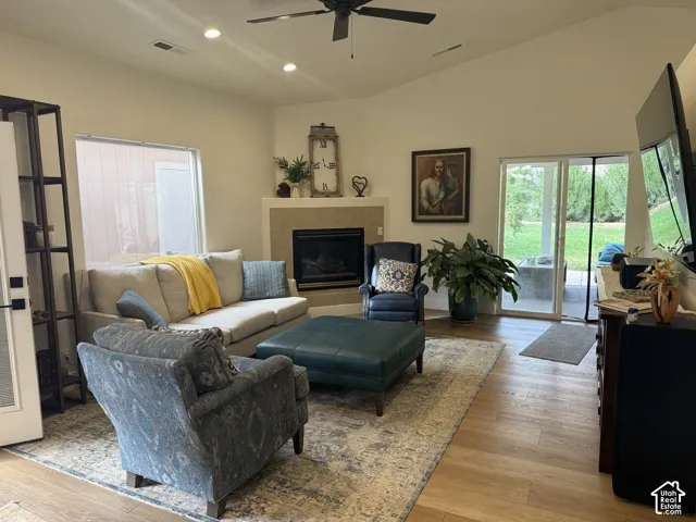 Spacious living room featuring hardwood flooring, a gas fireplace with surround mantel, ceiling fan, recessed lighting, and multi-panel glass doors providing natural light and access to outdoor space
