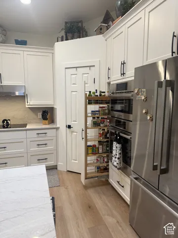 Kitchen featuring white shaker-style cabinetry, a slide-out spice rack, built-in stainless steel double ovens, wood-finish flooring, and stone countertops