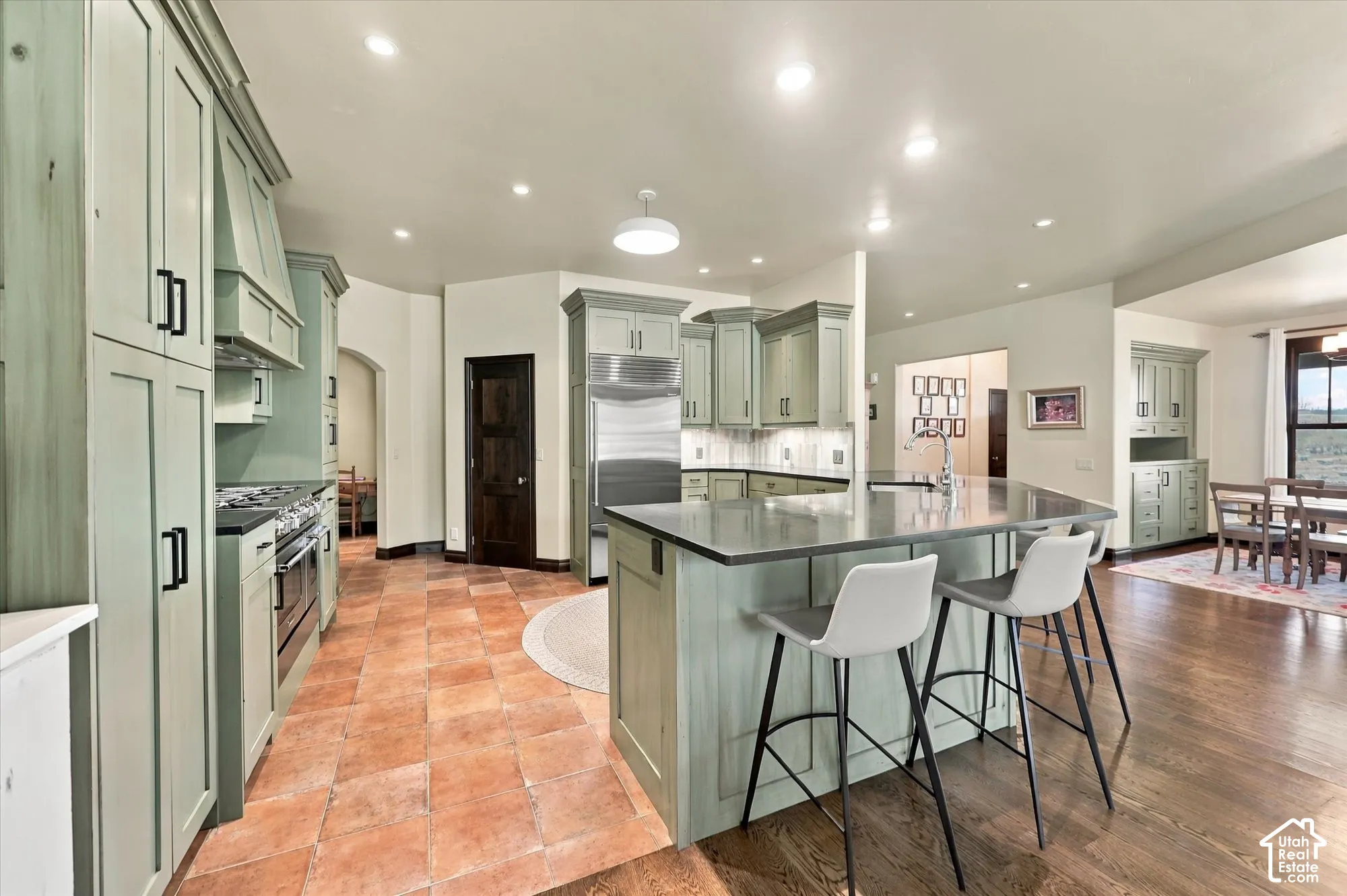 Kitchen featuring custom sage cabinetry, stainless steel professional-grade range, central island with solid-surface countertop, recessed lighting, and tile flooring